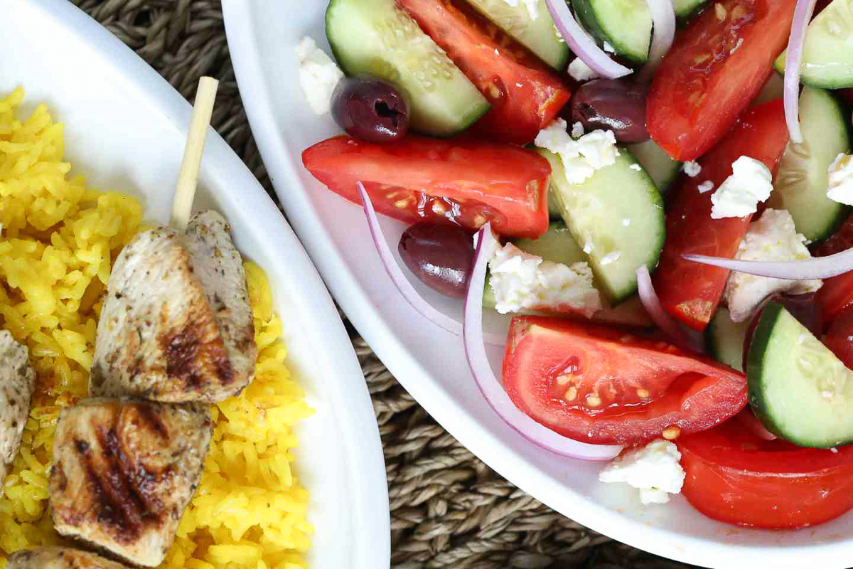 greek salad next to grilled chicken kabobs, both on white platters