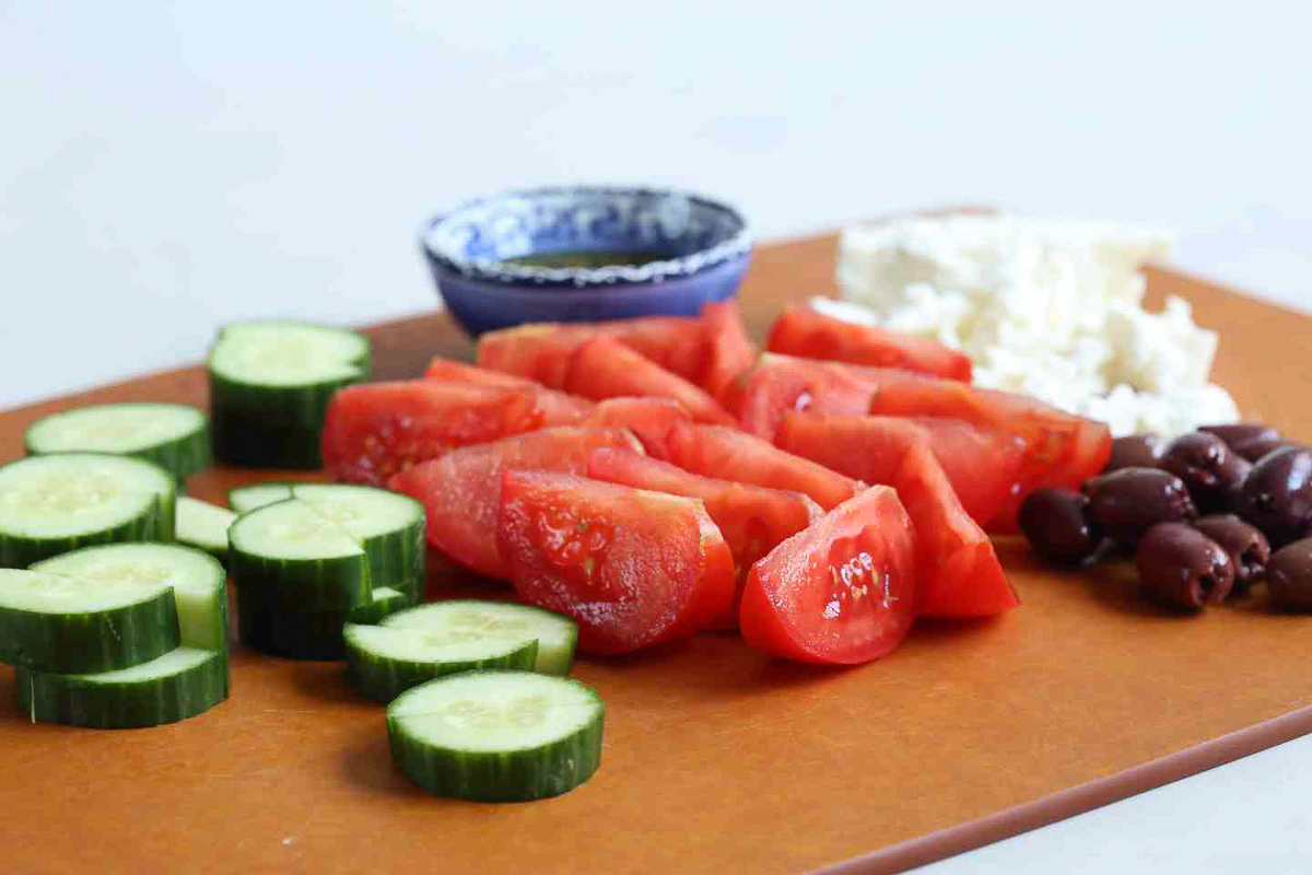 ingredients for greek salad with feta on a brown cutting board