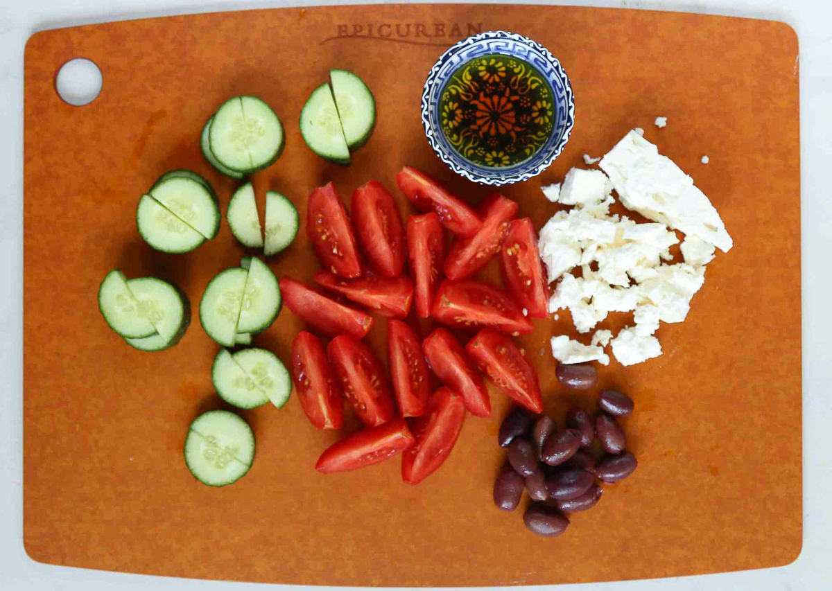 Greek salad ingredients on a brown cutting board.