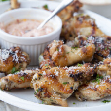 Grilled chicken wings on a white platter with a small bowl of sun dried tomato mayo