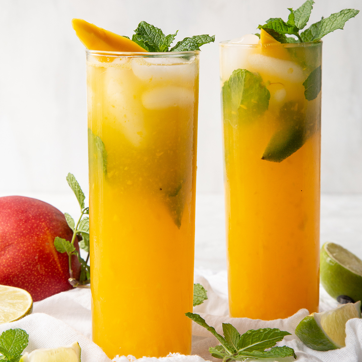 mango mojitos in glasses, garnished with mint and mango.