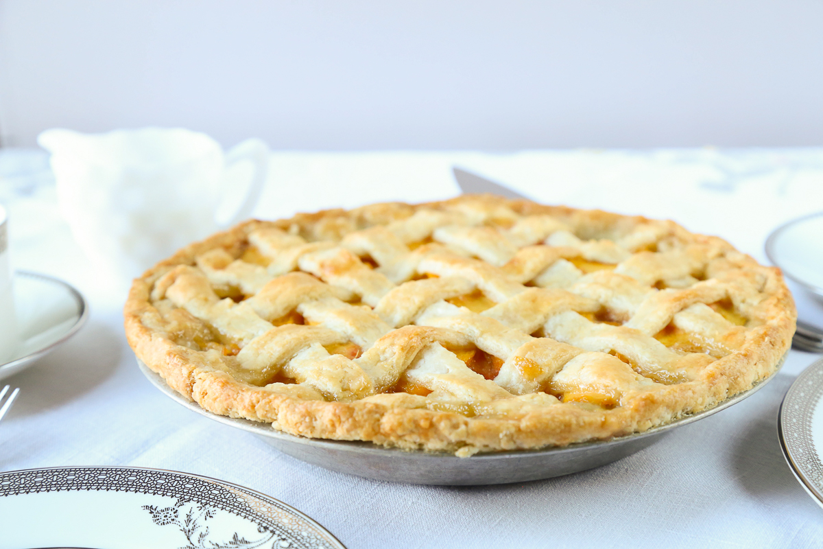 peach pie with a lattice crust on a white tablecloth.