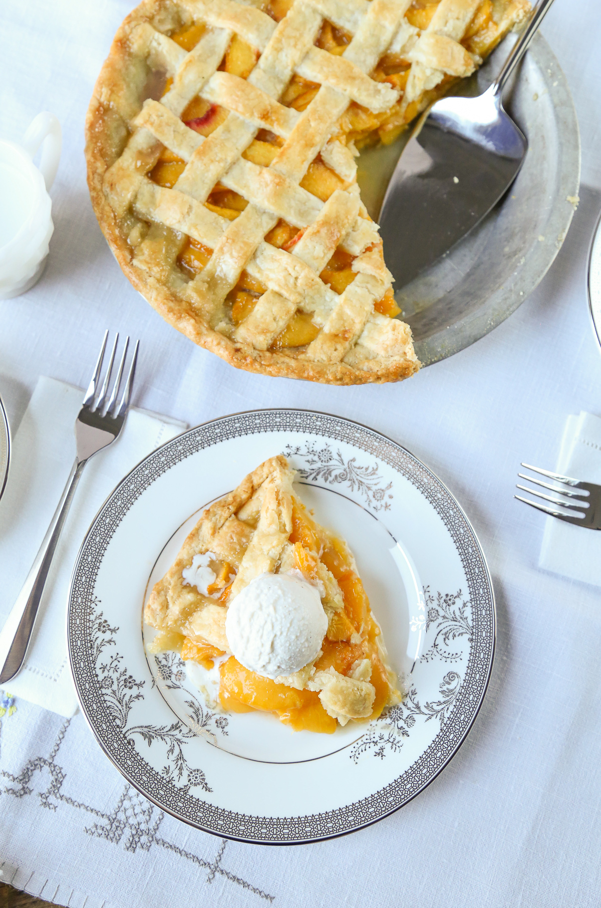 slice of peach pie on a china plate, with a whole peach pie in the background 