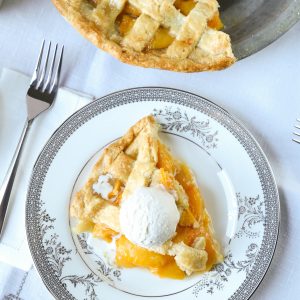 slice of peach pie on a piece of fine china with a fork on the side