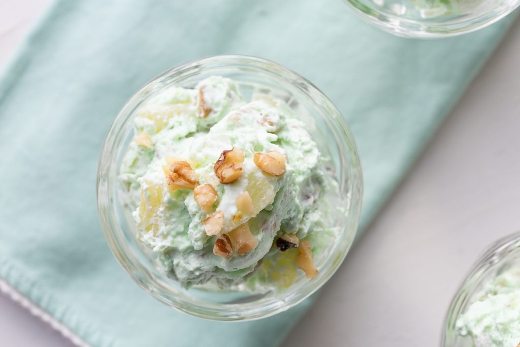 close up photo of pistachio pudding with walnuts in a glass dish, on a green cloth napkin