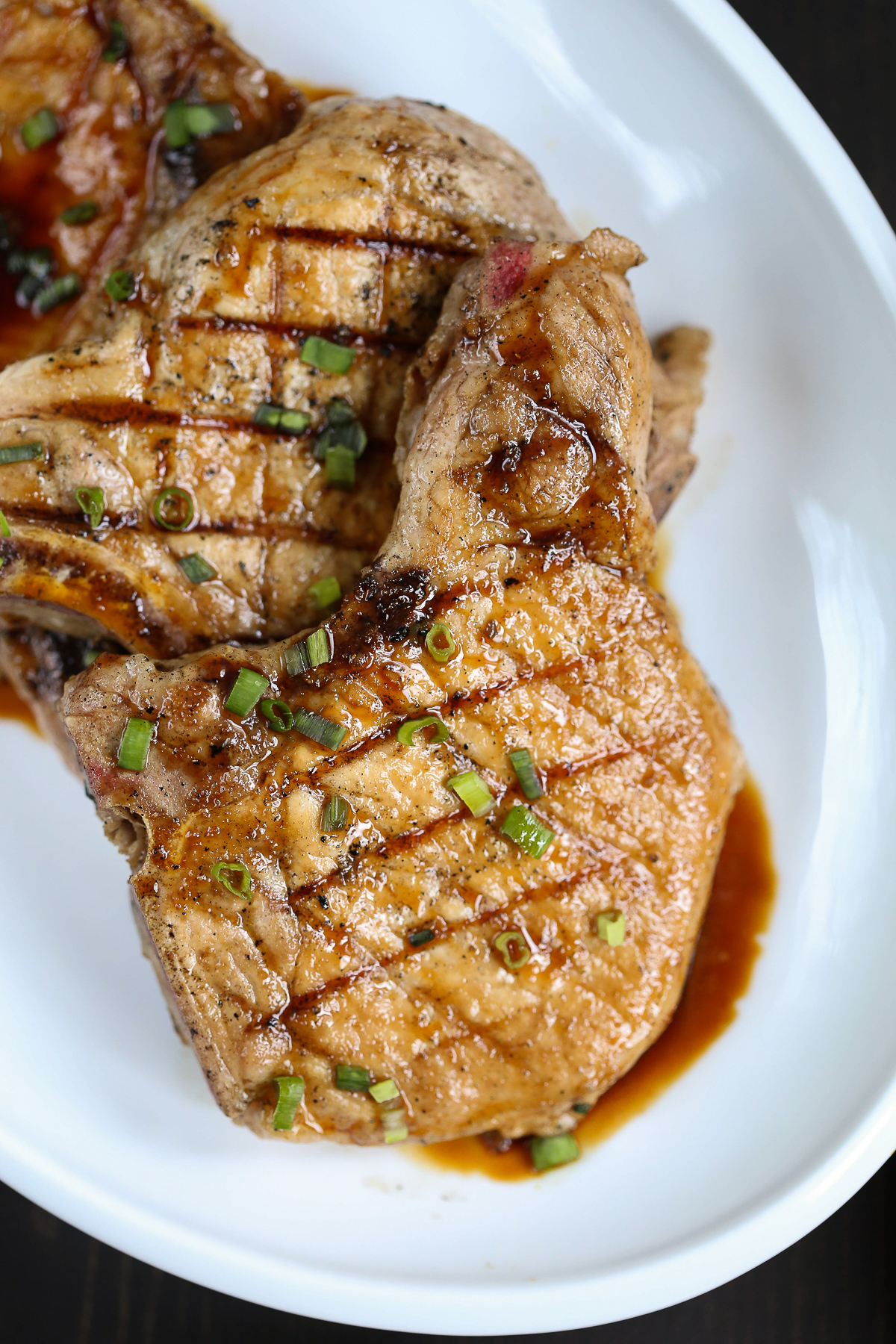 honey soy pork chops on a white platter topped with green onions.