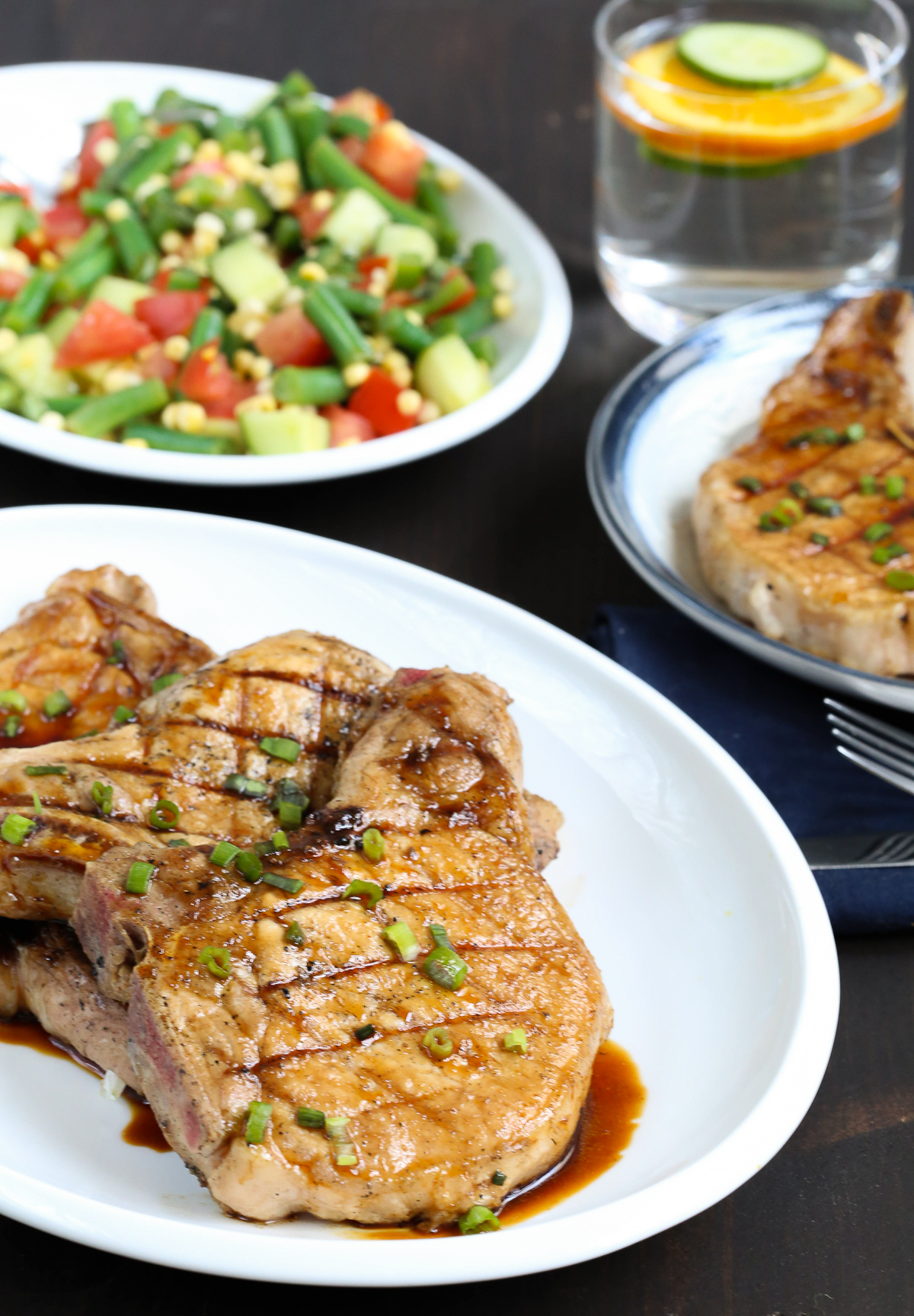 honey soy pork chops on a white platter with fresh vegetables in the background.