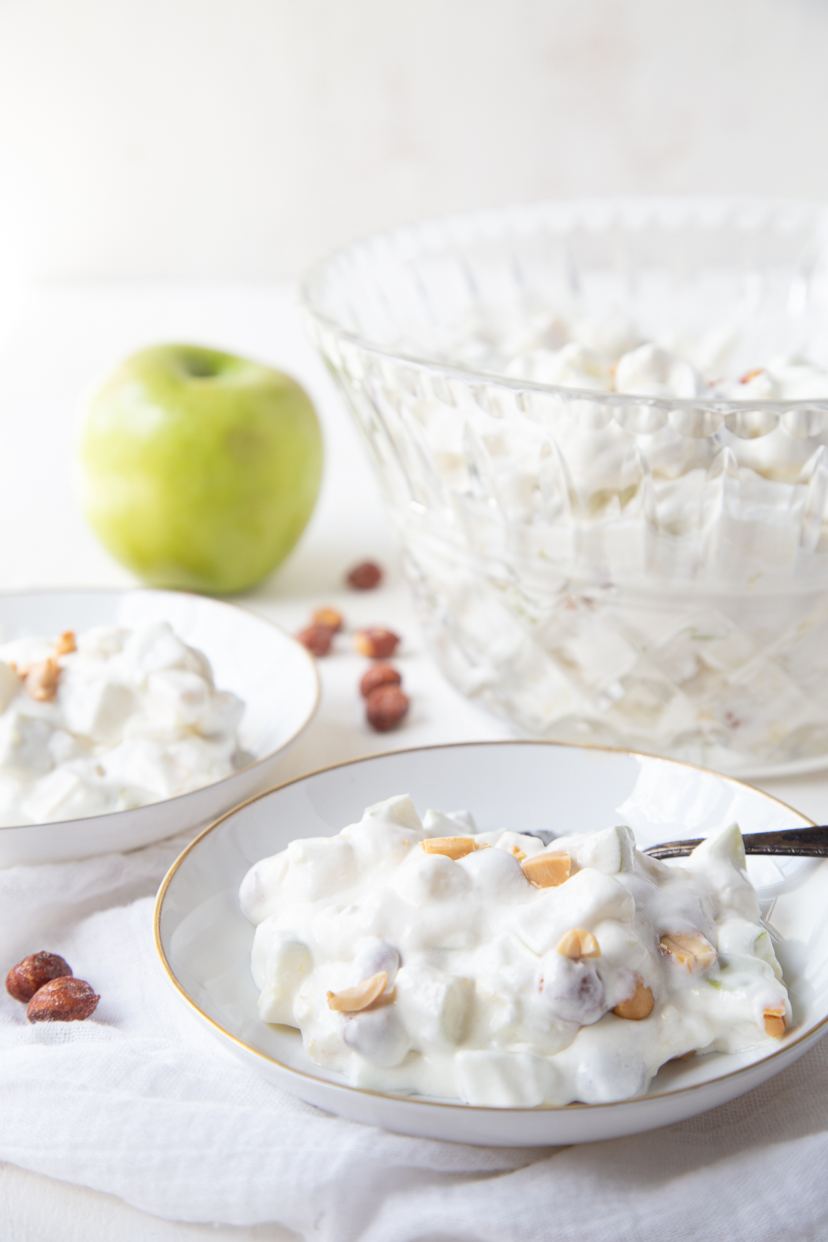 white shallow bowls filled with taffy apple salad next to a glass bowl and a green apple.