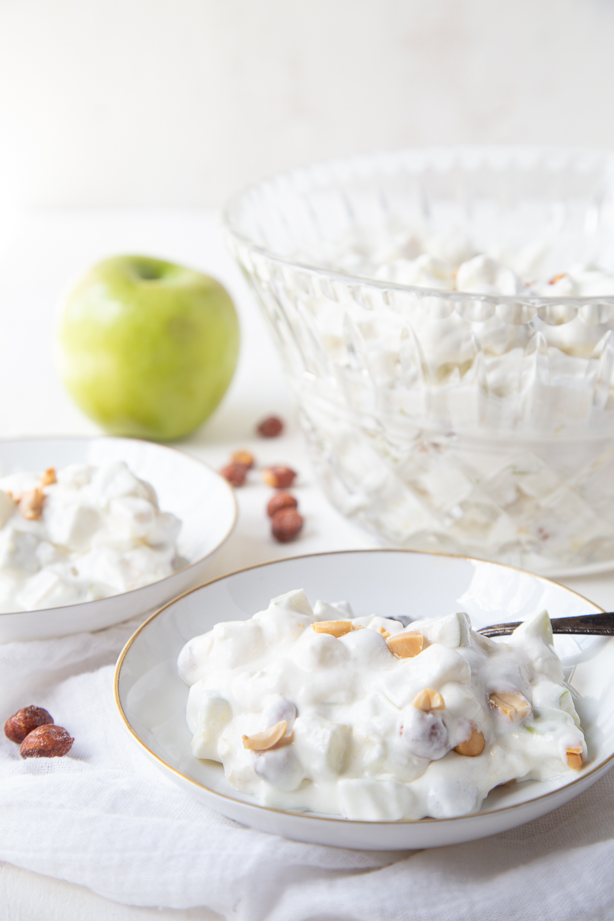 white shallow bowls filled with taffy apple salad next to a glass bowl and a green apple.