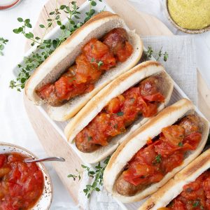 bratwursts in buns topped with tomato jam on a white rectangular platter