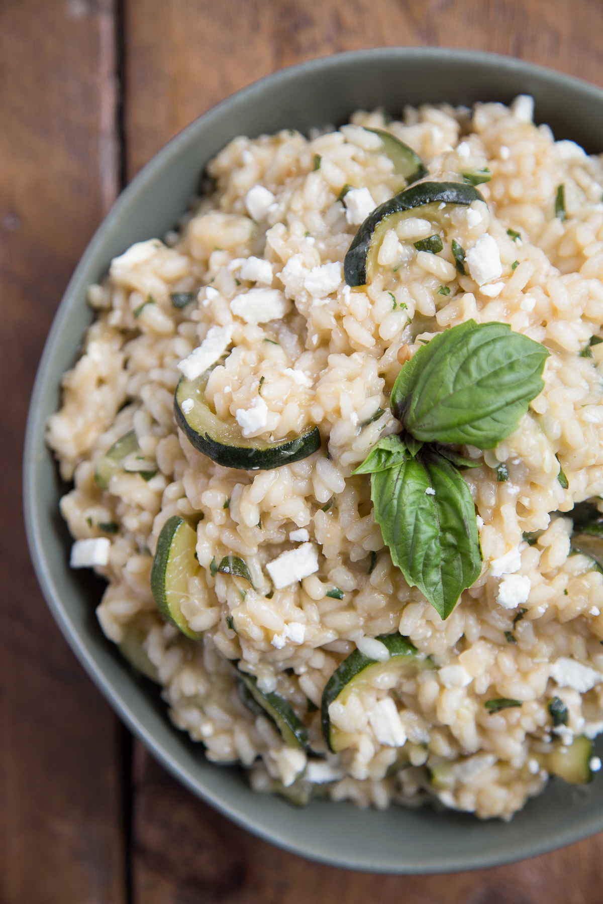 zucchini risotto with feta and fresh herbs in a green bowl on a wooden table