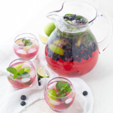 pitcher of blueberry mojitos surrounded by glasses filled with the mojito
