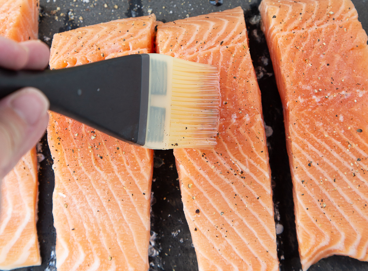 hand brushing salmon with oil using a silicone brush