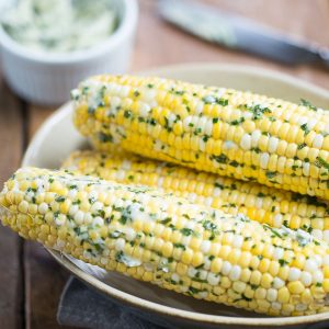 corn on the cob with herb butter sitting in a cream bowl