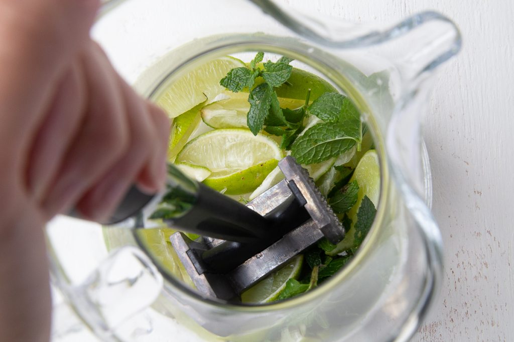 meat mallet smashing mint and limes in a glass pitcher