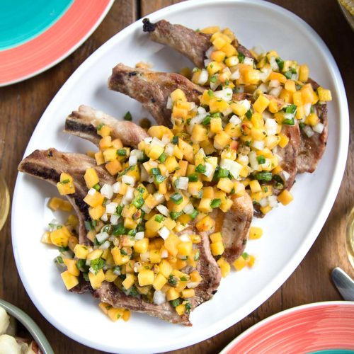 grilled pork chops with peach salsa on top, sitting on a white platter