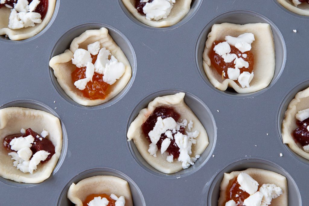 Puff pastry squares in muffin tin topped with goat cheese and jam