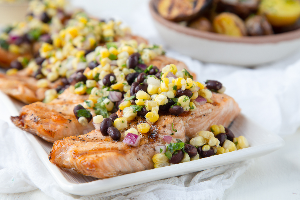 grilled salmon topped with corn salsa on a white platter