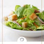 leafy green salad in a white bowl topped with croutons