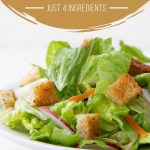 leafy green salad in a white bowl topped with croutons and radishes