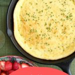 spoon bread in a cast iron skillet on a green tablecloth
