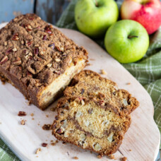 apple bread with slices cut out on a wooden board with apples in the background
