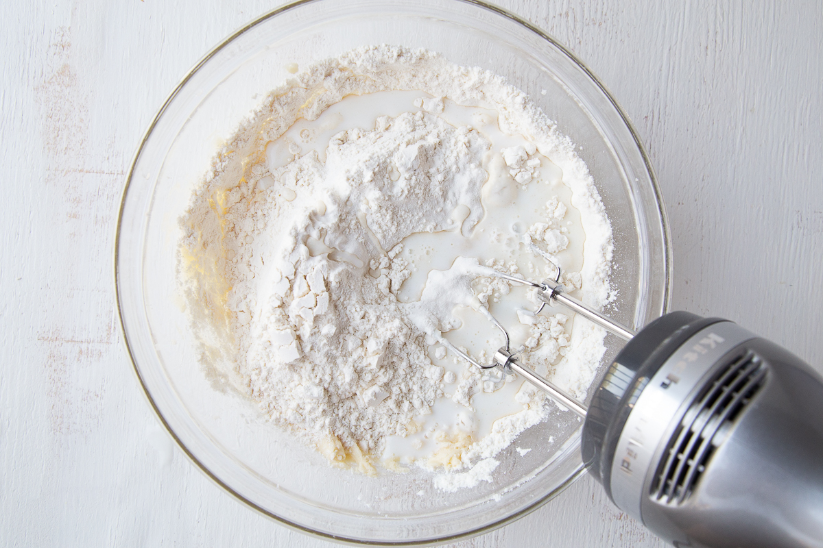 handheld mixer beating apple bread batter in a glass bowl