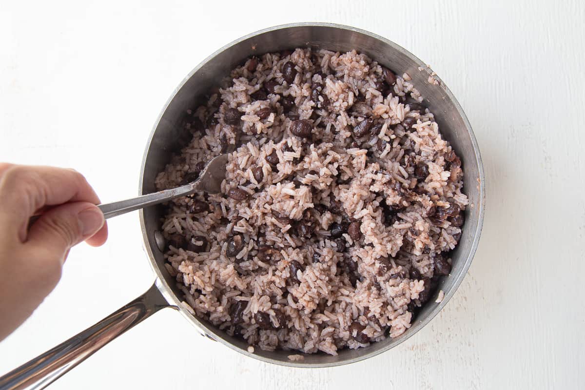 fork fluffing cuban black beans and rice in a saucepan.