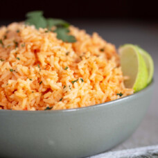 Mexican rice in a green bowl, garnished with slices of lime