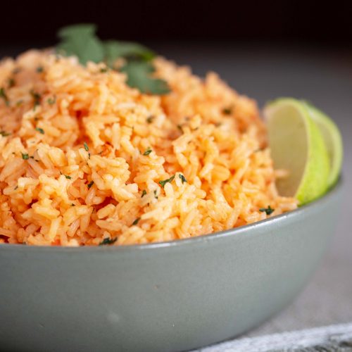 Mexican rice in a green bowl, garnished with slices of lime