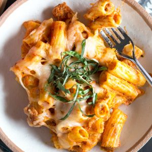 baked ziti in a cream bowl topped with basil