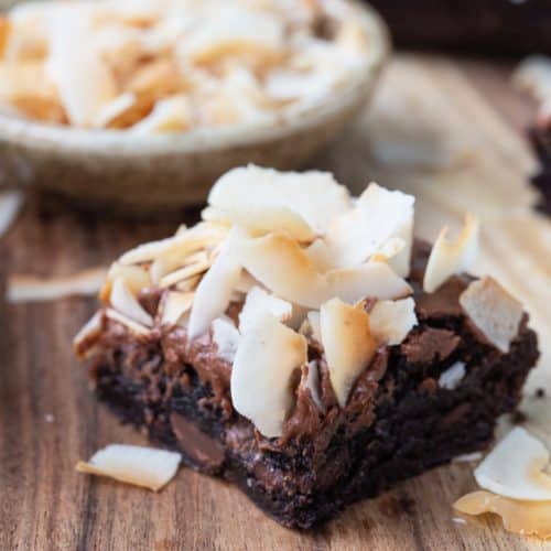 single brownie on a wooden board, topped with frosting and coconut curls.