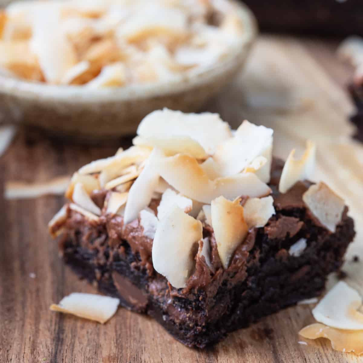 single brownie on a wooden board, topped with frosting and coconut curls.