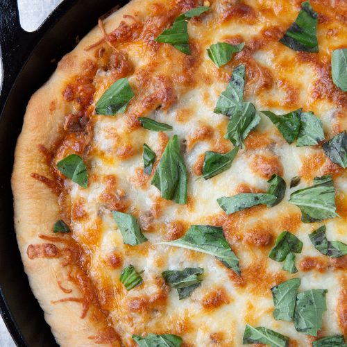 deep dish pizza in a cast iron skillet, topped with fresh basil