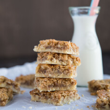 coconut bars stacked on parchment paper with a glass of milk