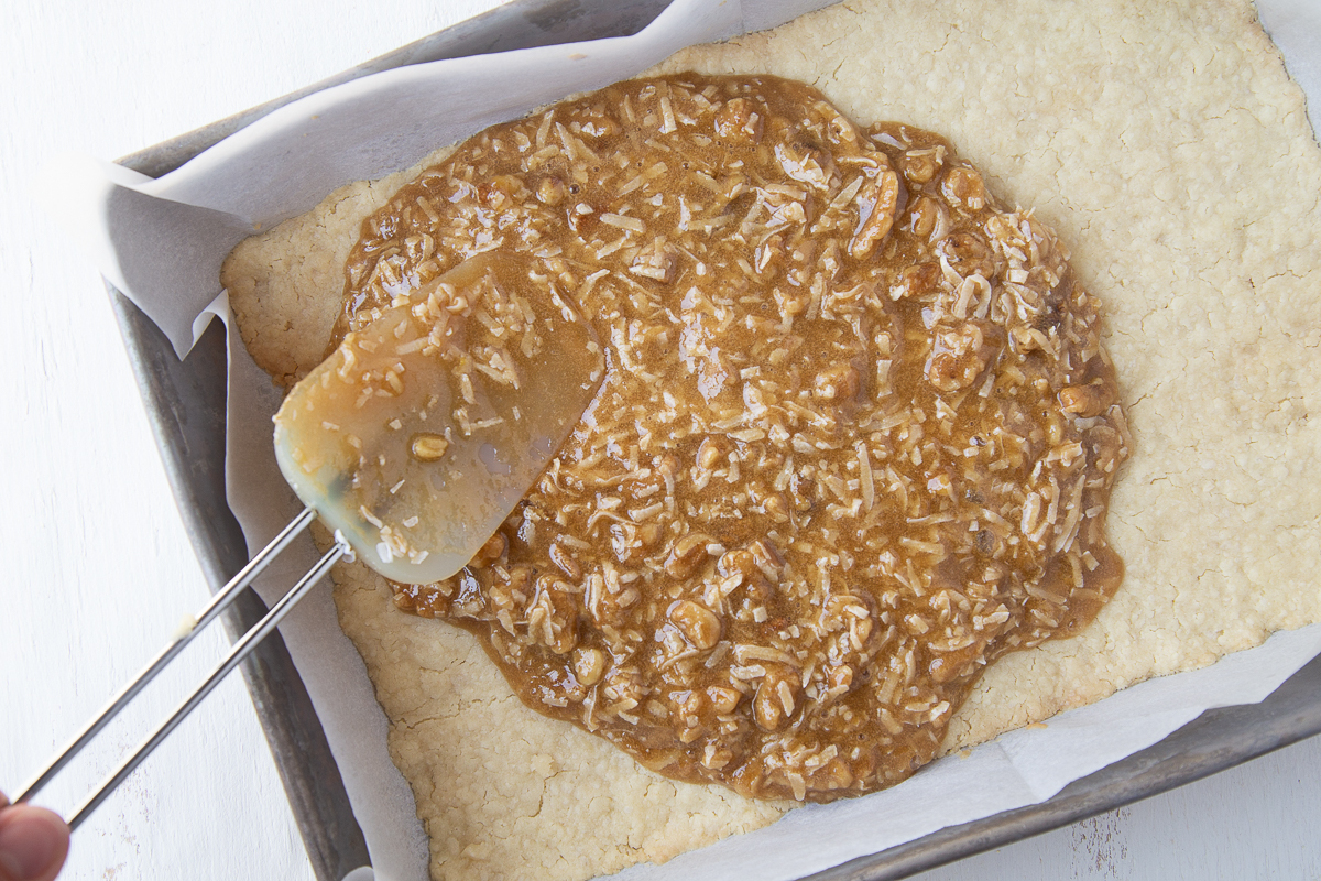 hand with a spatula spreading coconut filling onto crust in a 13x9 pan