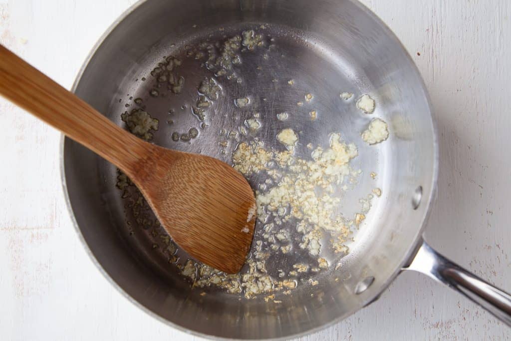 garlic frying in oil in a saucepan with a wooden spoon.