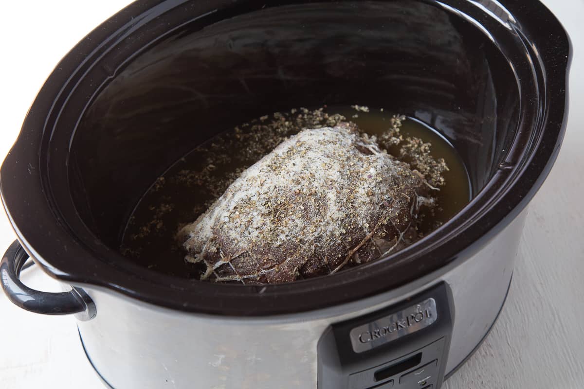 uncooked roast in a slow cooker surrounded by broth.