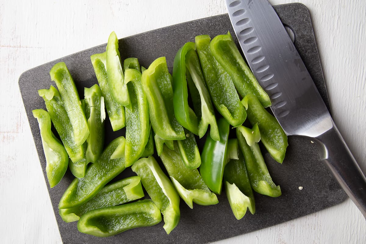 sliced bell peppers and a knife sitting on a black cutting board.