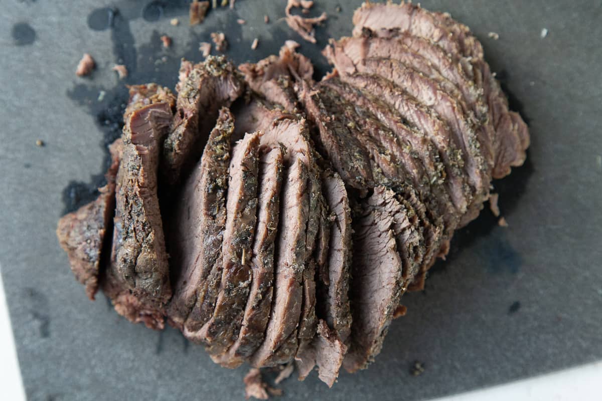 thinly sliced beef roast on a black cutting board