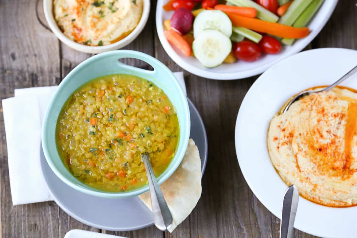 lemon lentil soup in a turquoise bowl on a wooden table with hummus and veggies