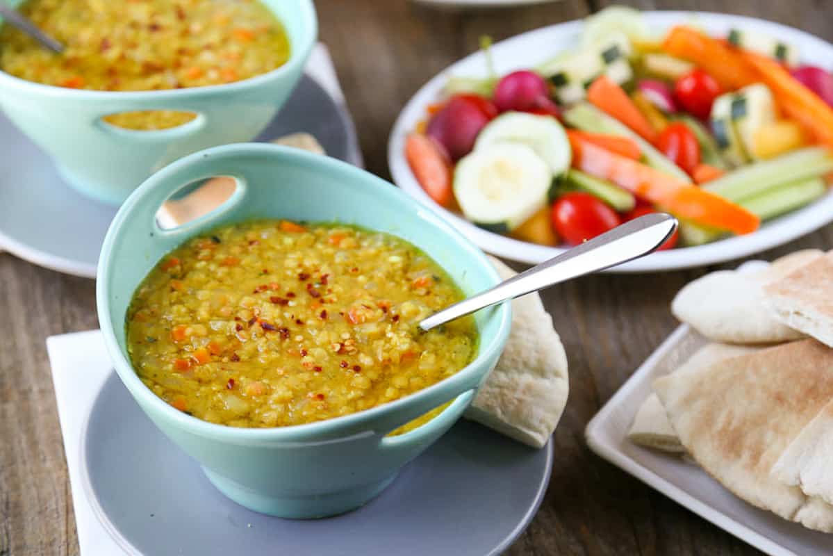 green bowl full of lebanese lemon lentil soup next to a platter of crudite.