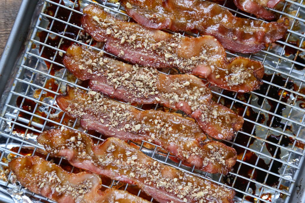 finely chopped pecans on top of bacon sitting on a wire rack