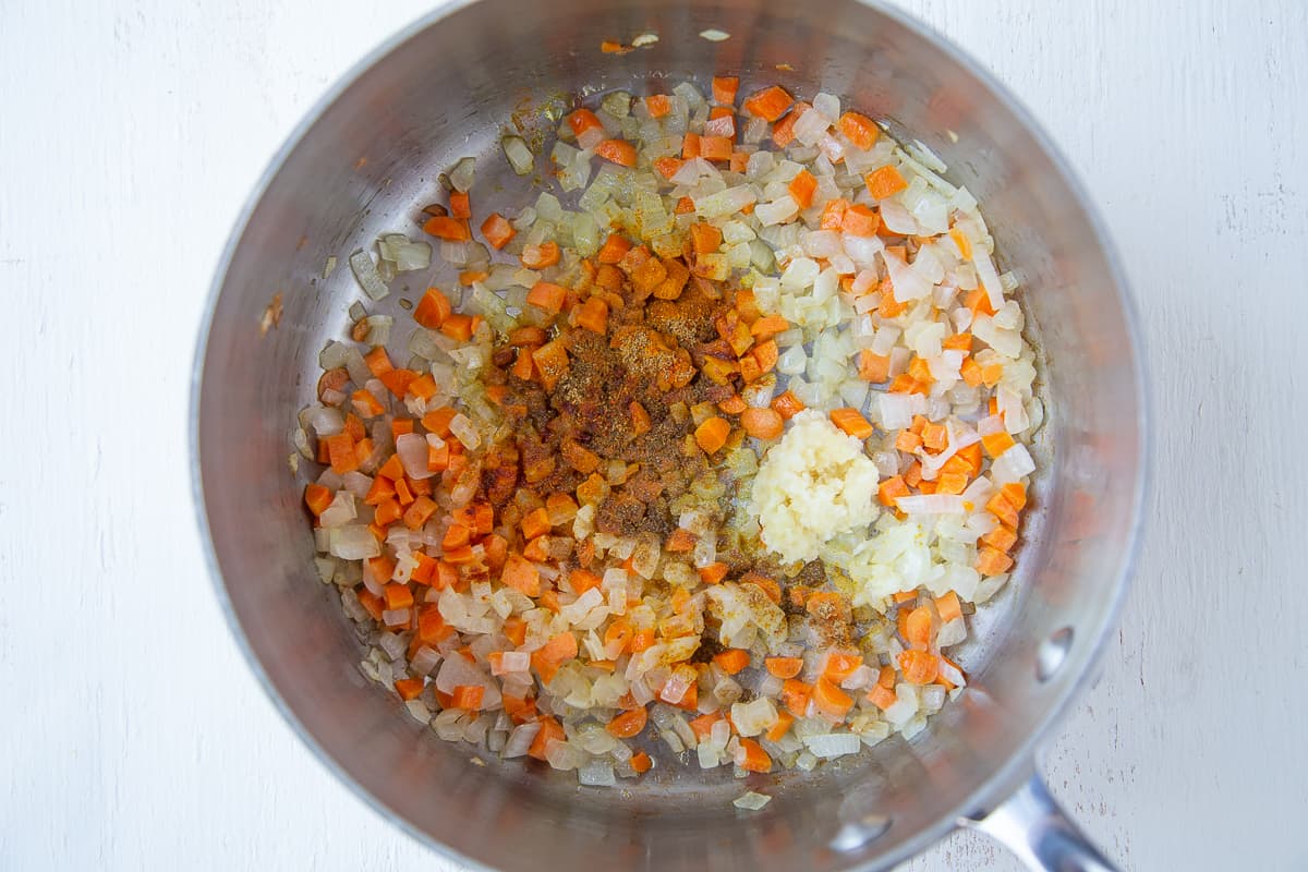 spices and garlic on top of sauteed carrots and onions in a pot.