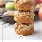 three apple muffins stacked on top of each other, with a muffin tin in the background.