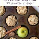apple muffins in a muffin tin with an apple, cinnamon stick, and nutmeg surrounding the muffins.