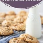 corn flake cookies on a white table with a glass of milk and a blue tea towel.