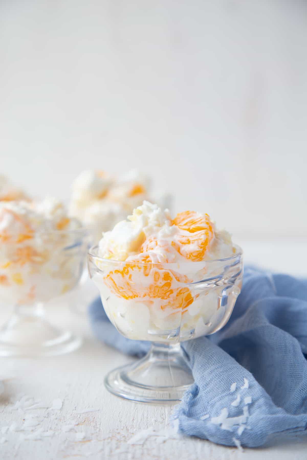 5 cup salad (ambrosia salad) in a small glass parfait bowl next to a blue cloth napkin.