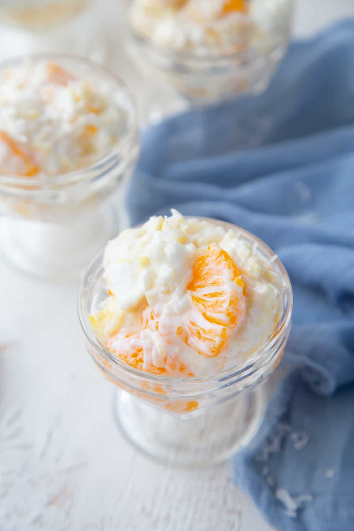 ambrosia salad in a glass parfait dish on a white table with a blue tea towel.