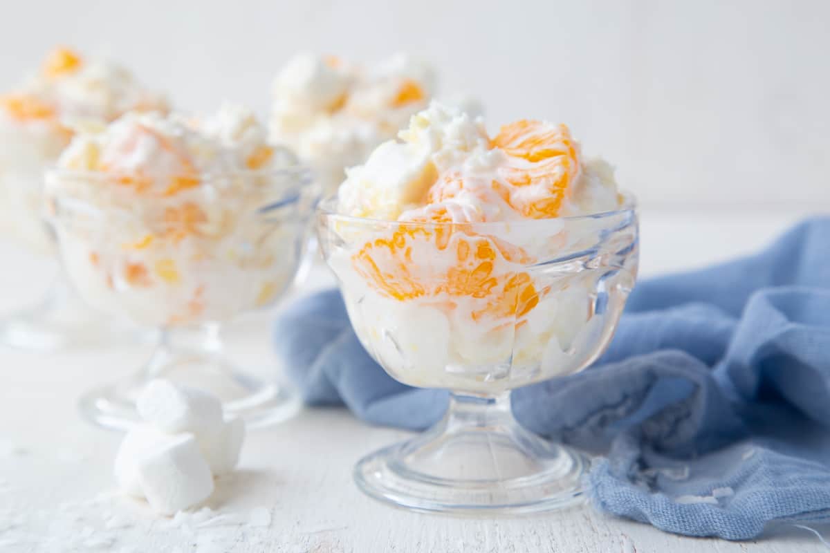 5 cup salad in a small glass parfait dish surrounded by mini marshmallows and a blue tea towel.